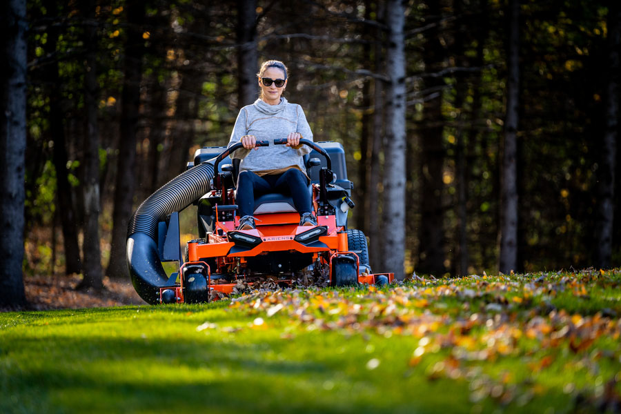 Home owner riding an Ariens zero-turn lawn mower with bagger, picking up leaves in a fall scene